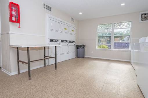 An onsite laundry facility with washers, dryers, a table for folding clothes, and a fire extinguisher at The Creole Apartments in Shreveport, LA