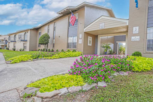 A leasing office with a US flag on it and a blooming garden bed in front  at The Creole Apartments in Shreveport, LA