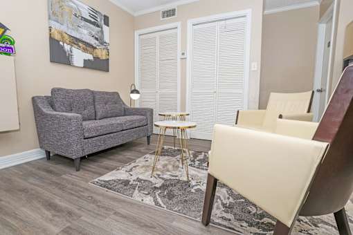 A grey couch sits in a leasing office with a small table and a chair at The Creole Apartments in Shreveport, LA