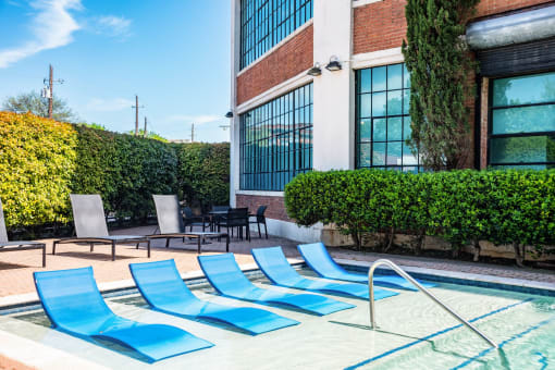 a pool with blue chaise lounge chairs in front of a brick building