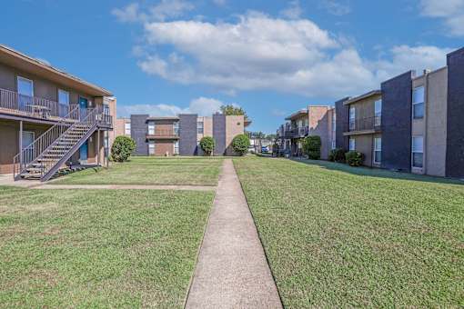 A grassy area in front of apartment buildings with a concrete walkway at The Drake in Bossier City, LA