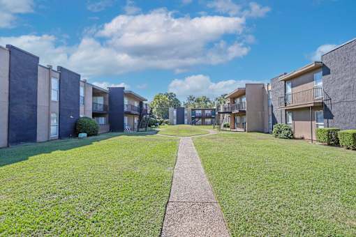 A row of modern apartment buildings with a sidewalk in the foreground at The Drake in Bossier City, LA