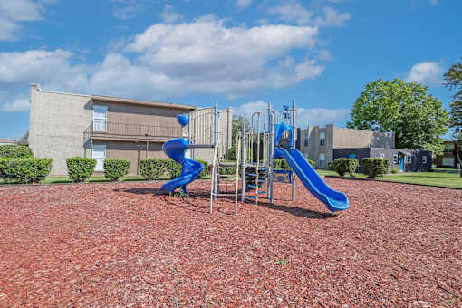 A playground with a blue slide and a red bark ground at The Drake in Bossier City, LA