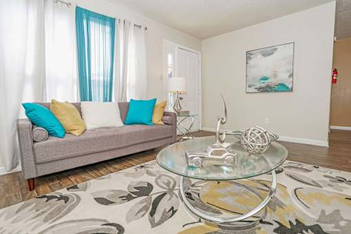 A living room with a grey couch and a glass coffee table at The Drake in Bossier City, LA