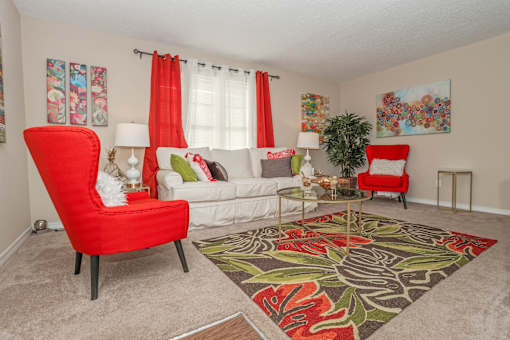Furnished living room with red seats and white couch, red curtains, and floral rug at Magnolia apartments in Shreveport, LA