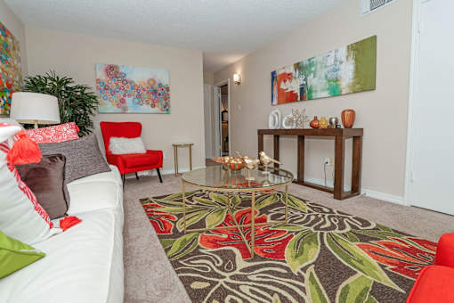 Furnished model living room with a white couch, red chair, and a glass coffee table at Magnolia Apartments in Shreveport, LA