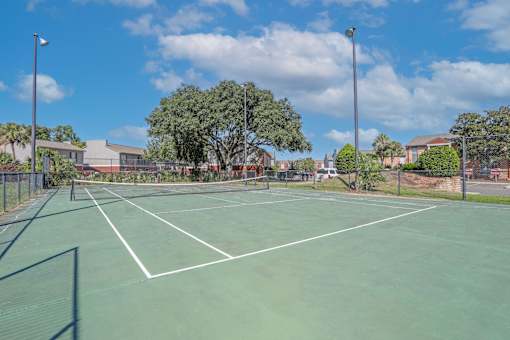 A tennis court surrounded by a fence and trees at Magnolia apartments in Shreveport, LA