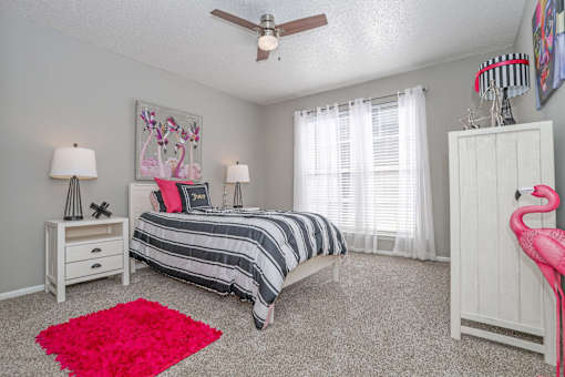 Model bedroom with a bed, nightstands, and a pink rug at Maplewood apartments in Shreveport, LA.
