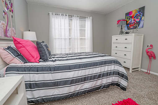 Model bedroom with a bed, nightstand, and a pink flamingo decoration at Maplewood apartments in Shreveport, LA.