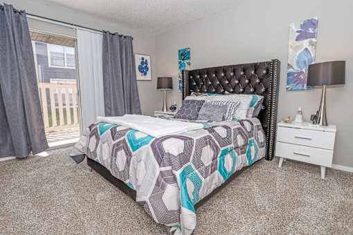Model bedroom with large bed and window letting in natural light at Maplewood apartments in Shreveport, LA.