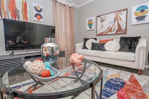 Model living room furnished with a couch, coffee table, TV, and paintings at Maplewood apartments in Shreveport, LA.