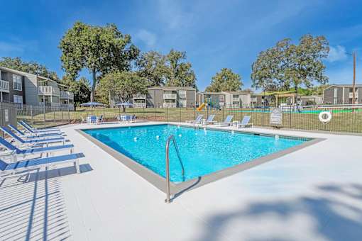 A swimming pool surrounded by sun loungers and trees at Maplewood apartments in Shreveport, LA.