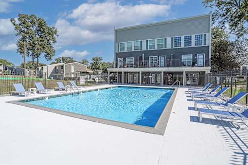 Our sparkling swimming pool behind the leasing office with white lounge chairs at Maplewood apartments in Shreveport, LA.