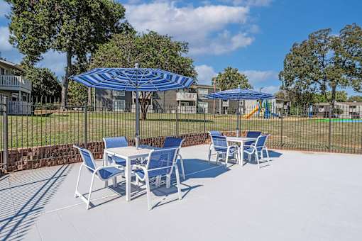 Poolside seating with blue and white striped umbrellas shading tables and chairs at Maplewood apartments in Shreveport, LA.