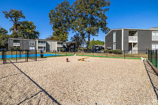 A dog park with a sandy area and a fence in front of apartment buildings at Maplewood apartments in Shreveport, LA.