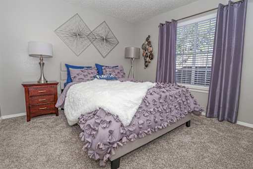 A bedroom with a bed, nightstand, and window at The Oasis apartments in Bossier City, LA