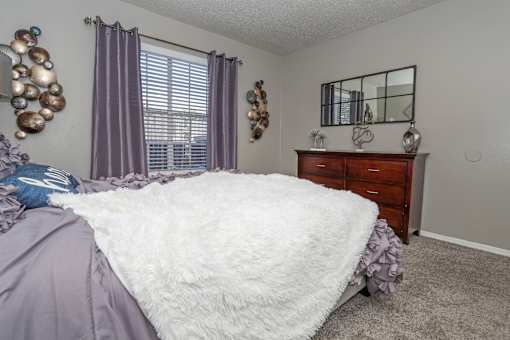 Ambassador bedroom with a large bed and a wooden dresser at The Oasis apartments in Bossier City, LA