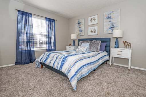 Model apartment bedroom with bed and blue curtains at The Oasis apartments in Bossier City, LA
