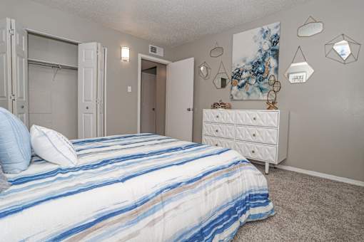 Model bedroom with a bed, dresser, and artwork on the wall at The Oasis apartments in Bossier City, LA
