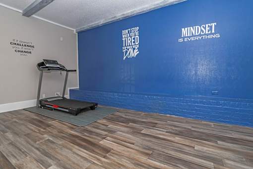 A treadmill is on a grey mat in a room with a blue wall at The Oasis apartments in Bossier City, LA