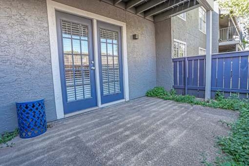 Model apartment concrete patio with a blue trash can and a blue fence at The Oasis apartments in Bossier City, LA