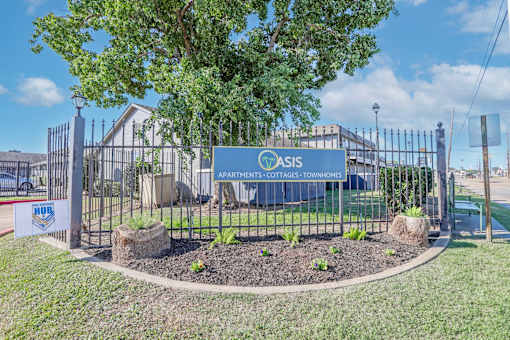 A sign for The Oasis with Apartments, Cottages, Townhomes is displayed in front of a fence at The Oasis apartments in Bossier City, LA