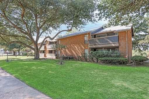 A red brick apartment building with a tree and well-manicured grass in front of it at The Pearl apartments in Shreveport LA