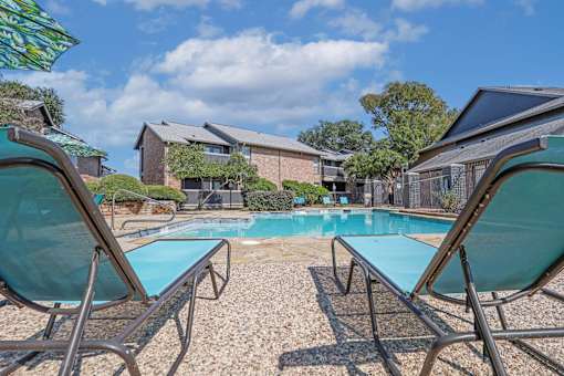 Blue lounge chairs by the pool with apartments in the background at The Pearl apartments in Shreveport, LA