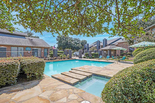 A swimming pool surrounded by a stone patio and green bushes At The Pearl apartments in Shreveport LA