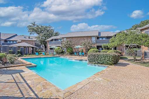 A swimming pool surrounded by a stone border and a residential area.