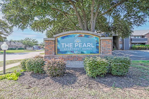A sign for The Pearl Apartment Homes stands in front of a tree.