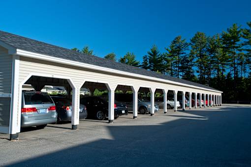 A long row of cars are parked under a covered parking structure.