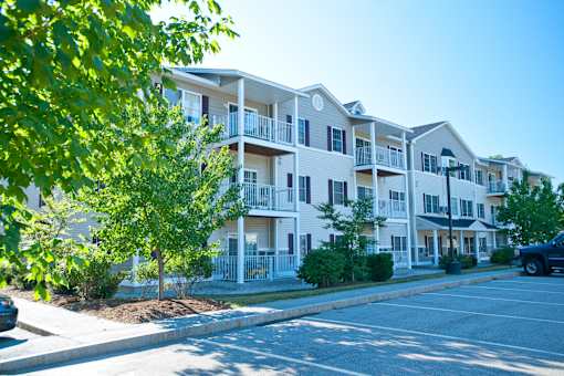 A row of white apartment buildings with green trees in the foreground.