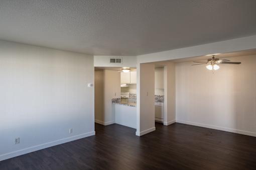 A room with a ceiling fan and a kitchen area in the background.