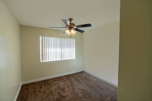 A room with a ceiling fan and a window with blinds.