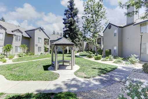 A gazebo sits in the middle of a grassy area in front of apartment buildings.