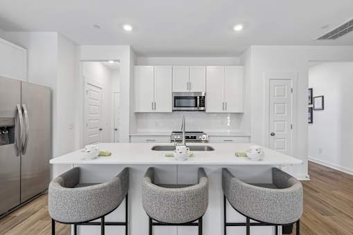 A modern kitchen with a white island and grey chairs.