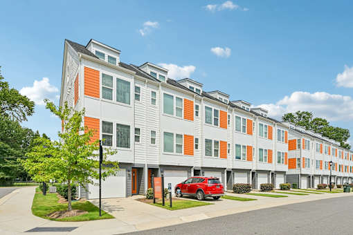 A red car is parked in front of a building with orange and grey panels.