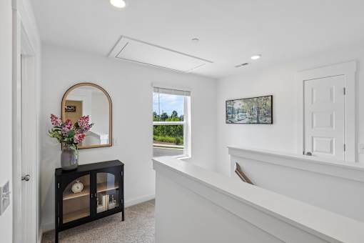 A room with a mirror, a vase with flowers, and a picture on the wall.