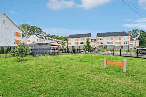 A grassy area in front of apartment buildings with a fence and orange barrier.