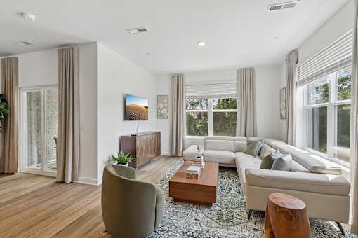 A modern living room with a grey sofa, a wooden coffee table, and a large window with curtains.