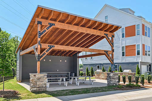 A wooden pavilion with a stone pillar and benches in front of a building.