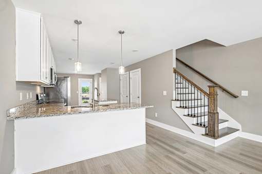 A modern kitchen with a marble countertop and a staircase with a wooden handrail.