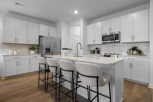 A kitchen with white cabinets and a white island with three chairs.
