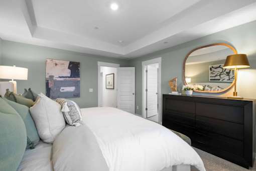 A bedroom with a large bed and a dresser with a lamp on top.