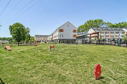 A red object is in the foreground of a grassy field with a white building in the background.