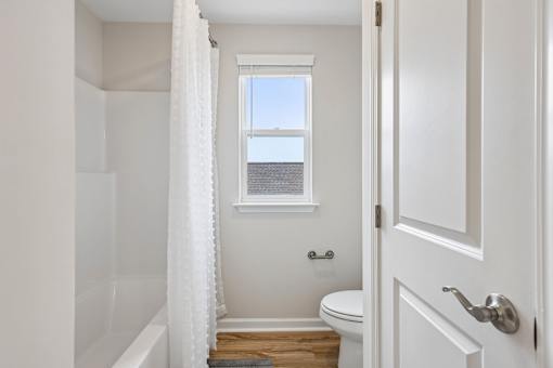 A white bathroom with a toilet, a tub, and a window.
