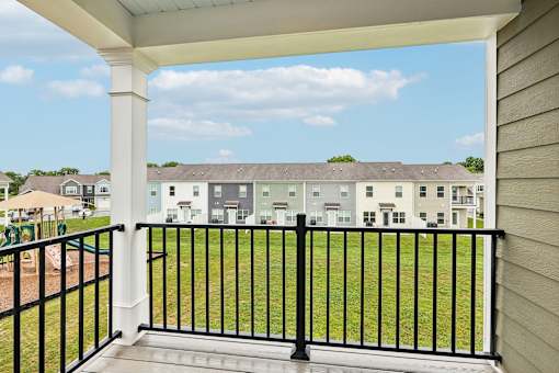 A balcony with a black railing overlooks a grassy area and buildings.