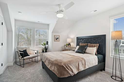 A bedroom with a bed, chair, and ceiling fan.