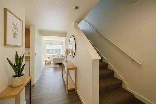 A hallway with a staircase and a mirror on the wall.